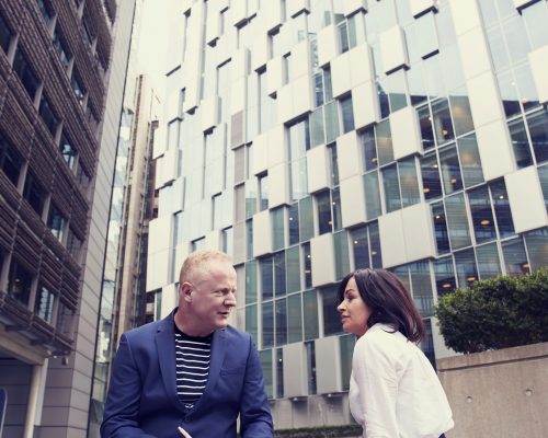 man-and-woman-sitting-on-wooden-bench-outside-buildings-2977513